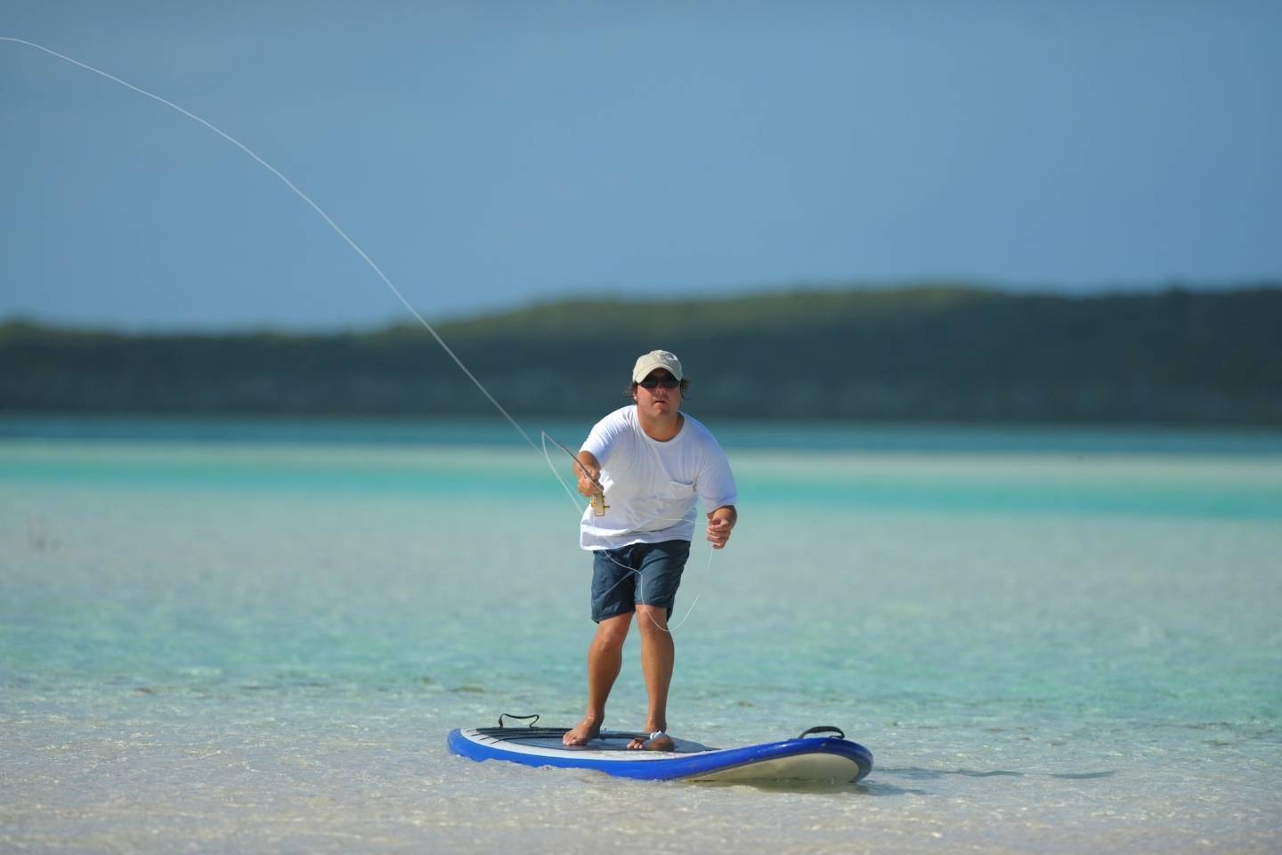 A man in white on paddle board with fishing gear
