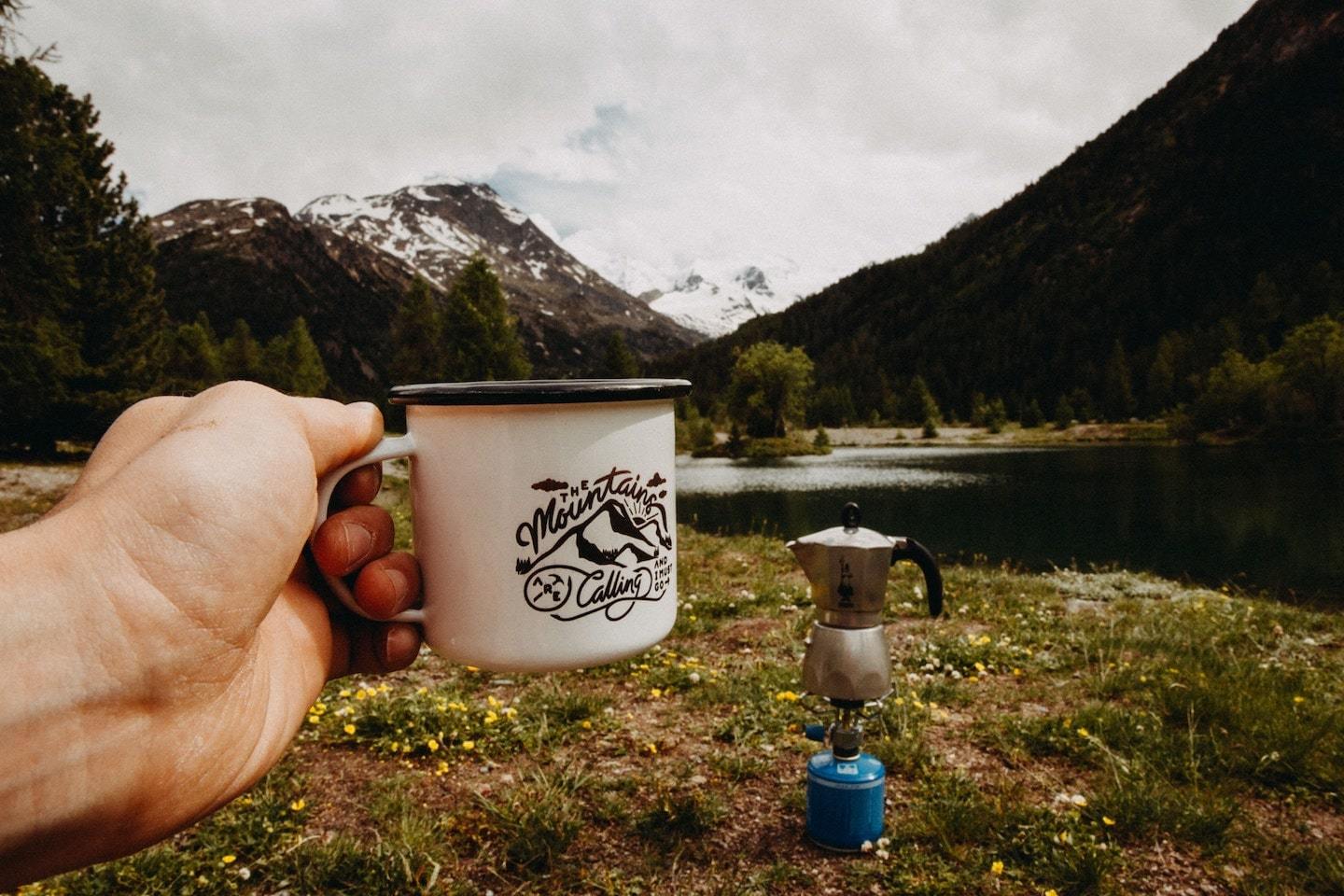 person holding mug at campsite in the mountains